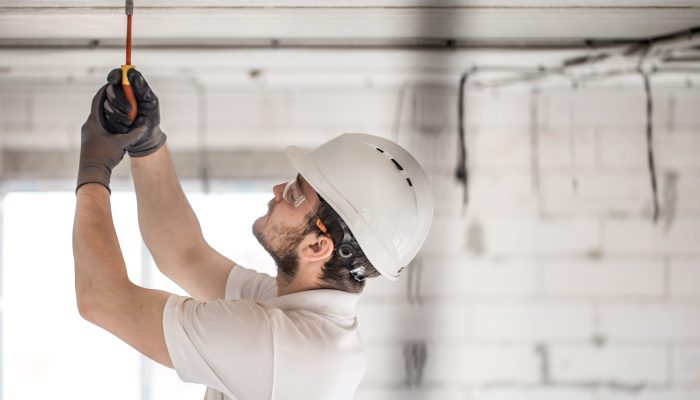 Electrician installer with a tool in his hands, working with cable on the construction site. Repair and handyman concept. House and house reconstruction.